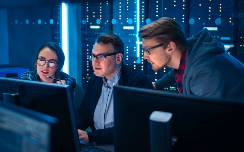 Hackers sitting around a table with computers on it displaying code